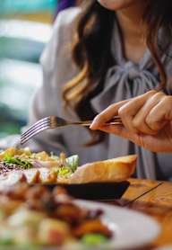 a woman sitting at a table eating food with a fork and knife