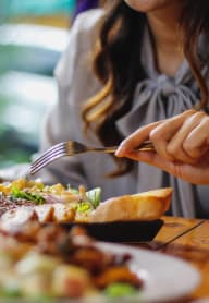 a woman sitting at a table eating food with a fork and knife