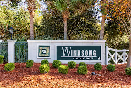 A sign that says "Windsong" is in front of a fence.
