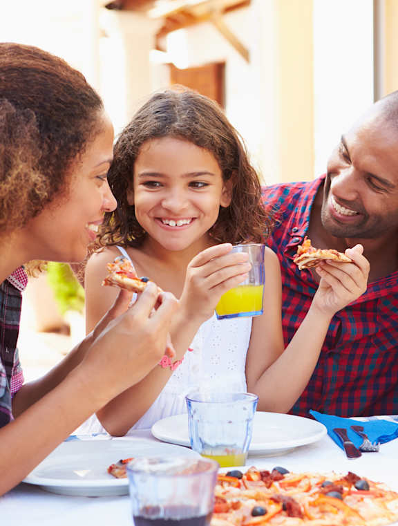 Four people eating pizza and drinking juice at a table at The Ranches at Gunsmoke, Maricopa, Arizona