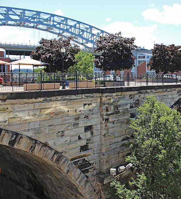 A stone bridge with a metal arch spans a road.