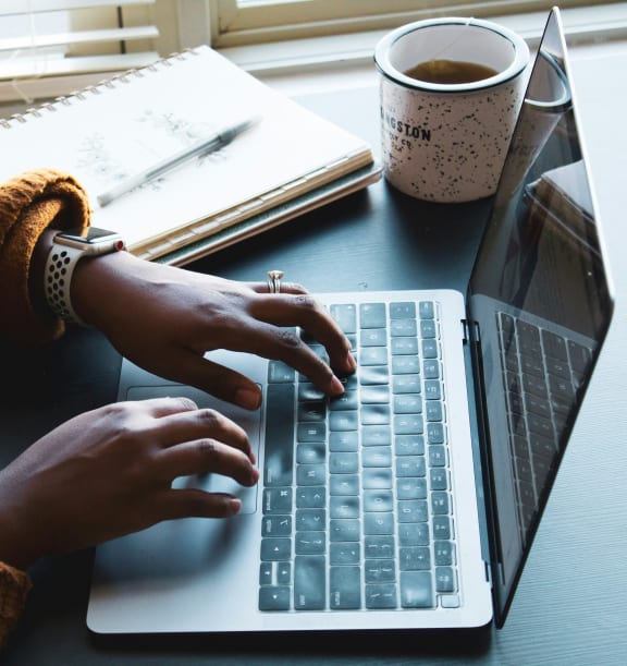 a woman typing on a laptop computer with a cup of coffee
