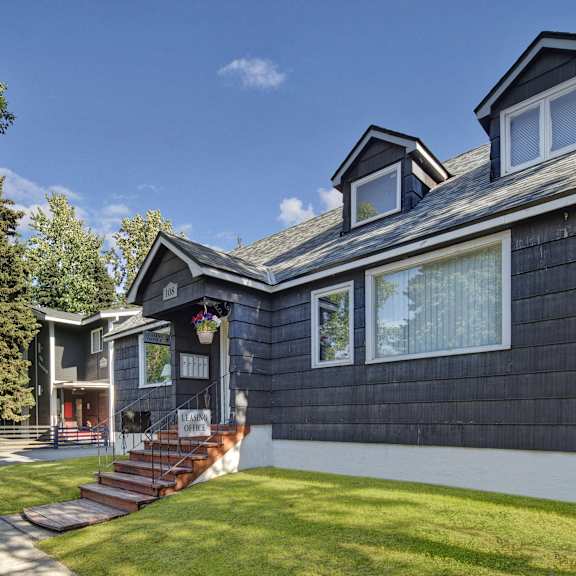 The front leasing office with brown stairs and potted plants surrounded by grass at the Alaskan Apartment Homes. 
