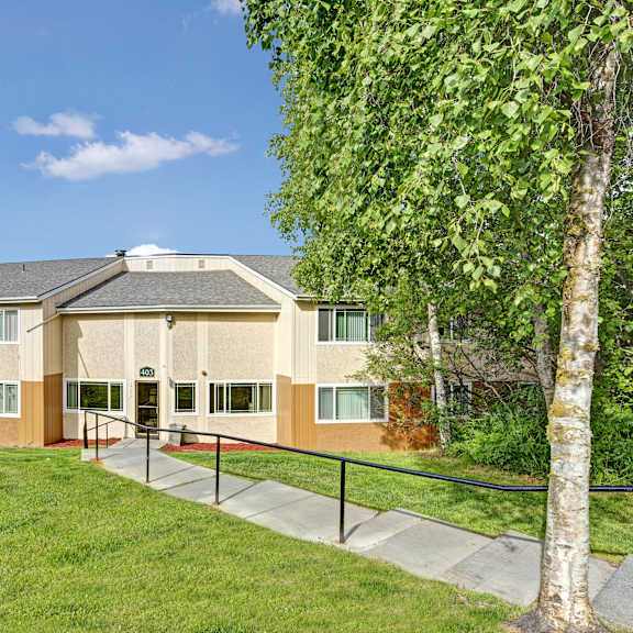 The stunning pathways surrounded by grass and trees leading to an apartment building at Taiga Apartment Homes.