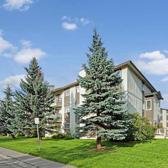 The exterior of the apartments and the green space with grass, trees, and shrubs at the Legacy West Apartment Homes.