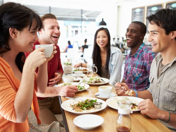 a group of people sitting around a table eating food and drinking coffee