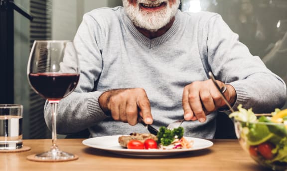 a man eating food at a table with a glass of wine