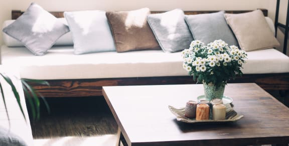 Wooden couch with neutral throw pillows next to coffee table with flowers