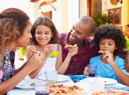 Four people eating pizza and drinking juice at a table.