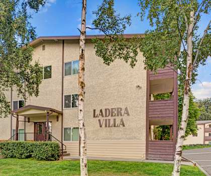 The exterior sign and building of Ladera Villa surrounded by trees and greenery. 