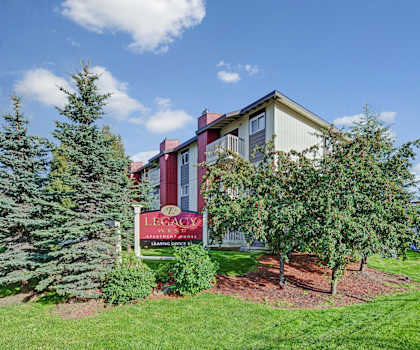 The exterior sign, building, and parking lot with trees and greenery of the Legacy West Apartment Homes.