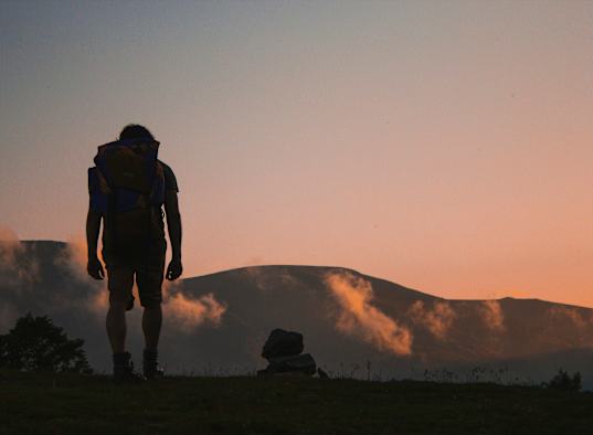 A man with a backpack stands on a hill.