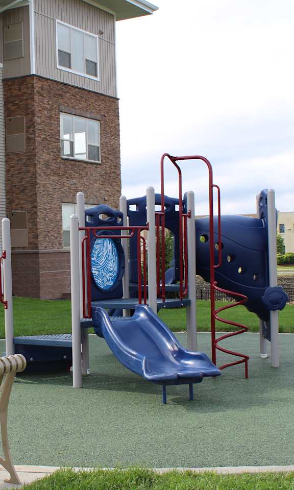 A playground with a slide, swings, and a bench in front of a building.