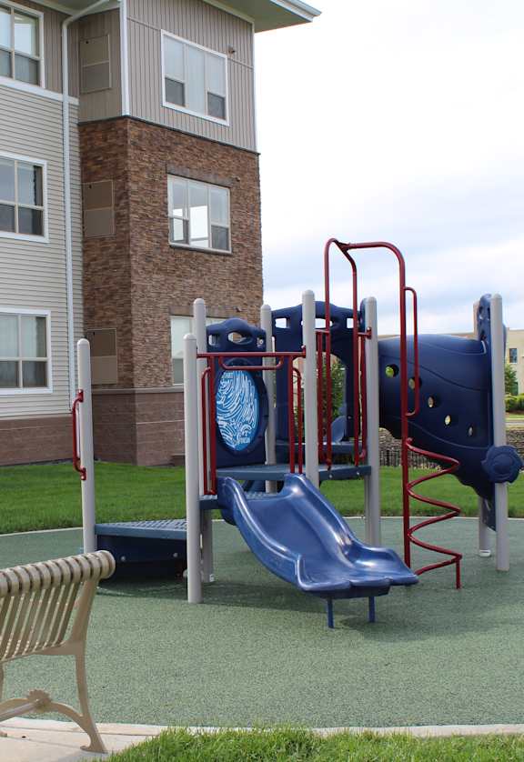 A playground with a slide, swings, and a bench in front of a building.