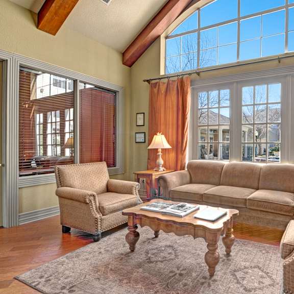 The amazing resident lounge with couches, decorations, large windows with curtains, plush chairs, and coffee tables at Woodland Park Apartment Homes. 