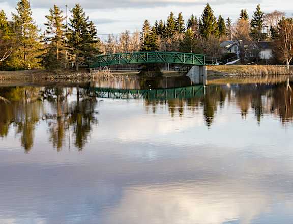 A green bridge over a calm body of water with trees in the background.