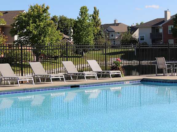 a swimming pool with chairs and a fence with houses in the background