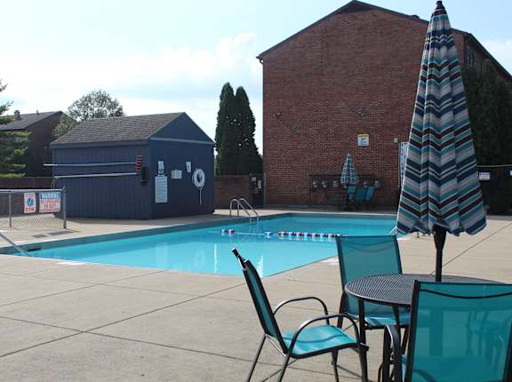 our swimming pool in front of our house with chairs and an umbrella