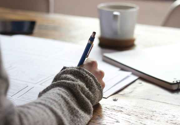 a person writing on a piece of paper with a pen