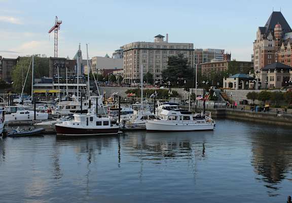 A marina with boats docked in the foreground and buildings in the background.