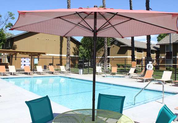 A pool with a red umbrella and chairs around it.