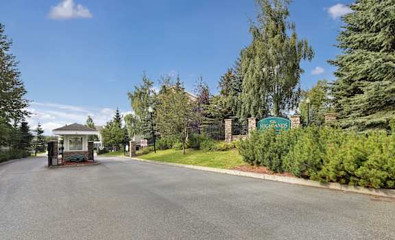 The road leading to the front entrance with a green sign surrounded by trees and bushes at the Highlands Luxury Residences Apartment Homes. 