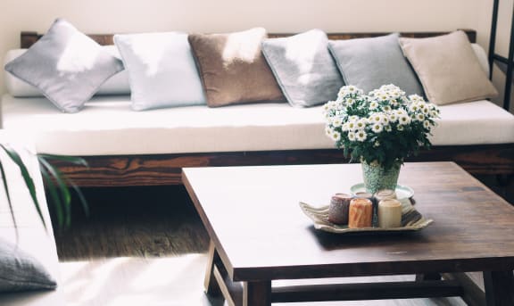 Wooden couch with neutral throw pillows next to coffee table with flowers