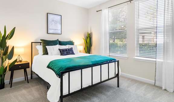 A bed with a green blanket and white pillows in a room with a window.