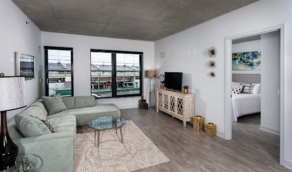 A living room with a grey couch, a glass coffee table, a white cabinet, and a large window. at Residences at Addison Clark, Chicago, IL, 60613