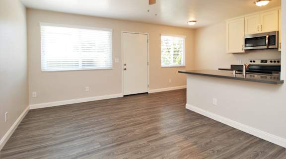 an empty living room with a kitchen and a ceiling fan