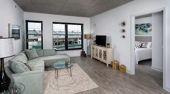 a living room with a gray couch and a glass coffee table and sliding glass doors at Residences at Addison Clark Apartments, IL, 60613