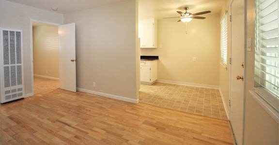 an empty living room with a ceiling fan and a kitchen