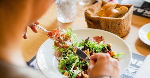 A person eating a salad with a fork and knife.