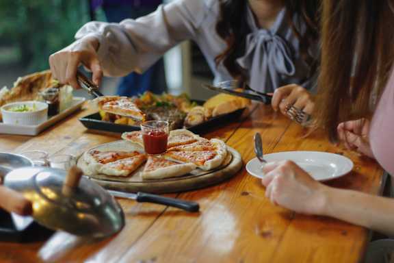 A person is cutting a pizza with a knife and fork.