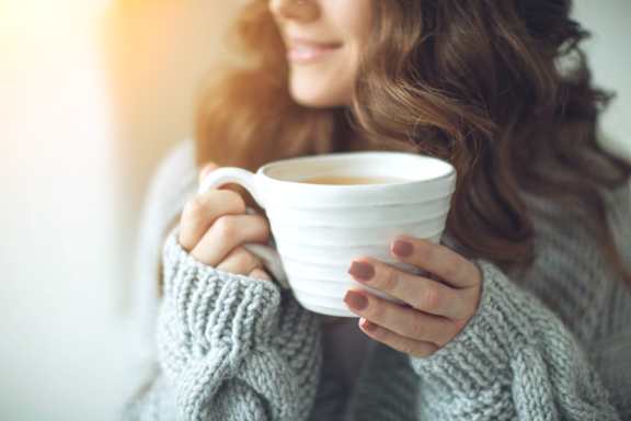 A woman in a grey sweater is holding a white cup.at Station Village at Denville, Denville, NJ