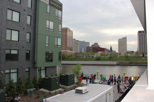 a crowd of people are gathered on a sidewalk next to a river with buildings in the background