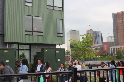 a crowd of people sit on a bench in front of green buildings and a body of water