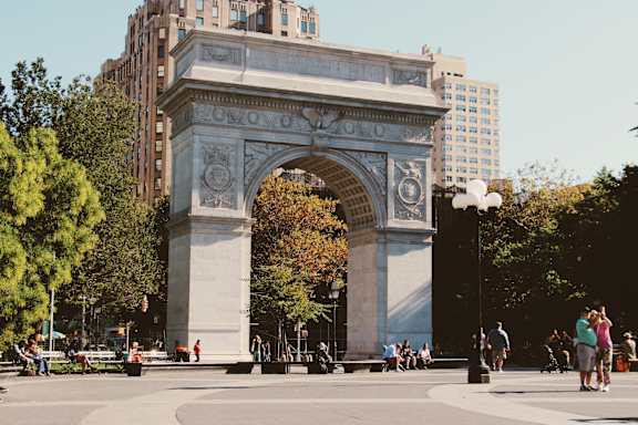A large archway in a city square with people walking around it.