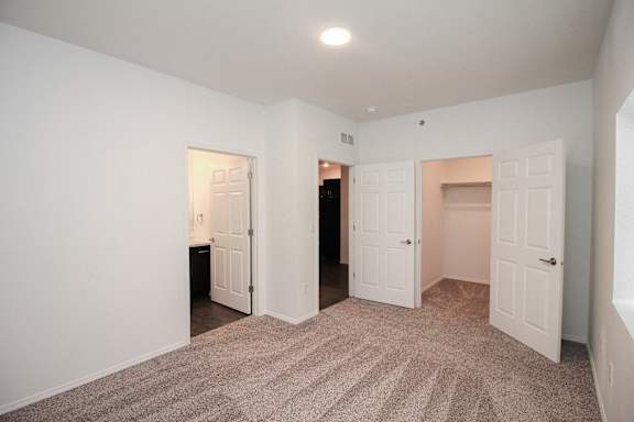 A room with carpeted flooring and white walls with three doors.