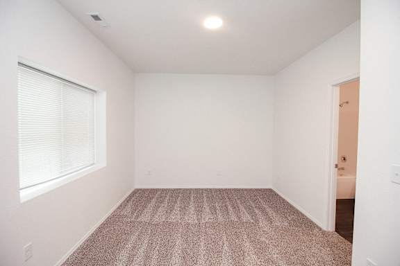 A room with a carpeted floor and a window with blinds.