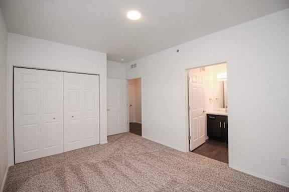 A room with white walls and a carpeted floor with a door open to a kitchen.