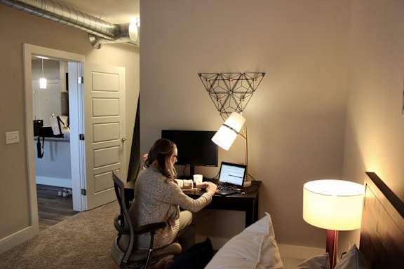 a woman sitting at a desk with a laptop and a lamp at CityWay Apartments, Indianapolis