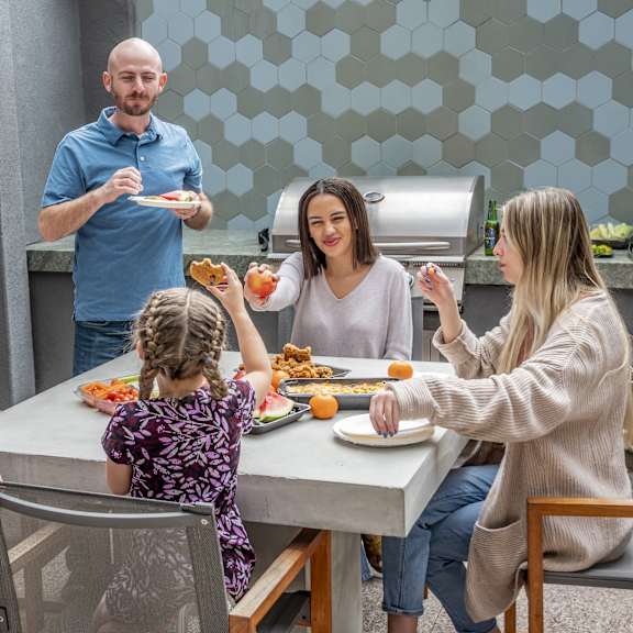 A family sitting around a dining table by a grill eating food at Edgewood Estates Apartment Homes. 