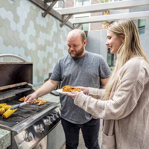 A man and a woman cooking food on a grill at Gateway Gardens Apartment Homes.