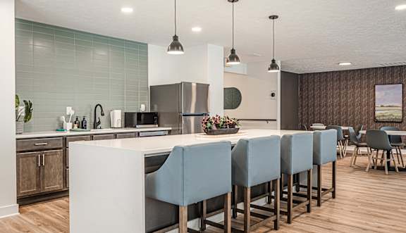 A modern kitchen with a long white island and blue chairs.