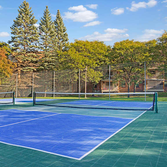 A blue and green tennis court with a fence and trees at Plymouth Square.