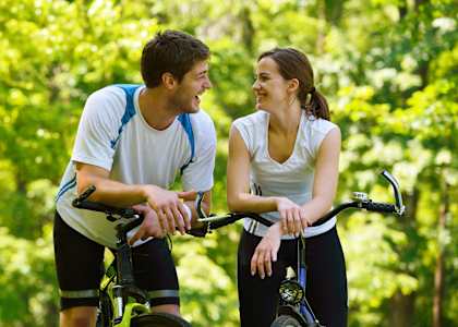A man and a woman are riding bicycles together in a forest.