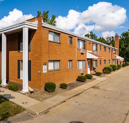a brick apartment building with white columns and a sidewalk