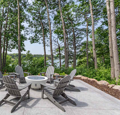 a patio with a firepit and chairs with a view of the water