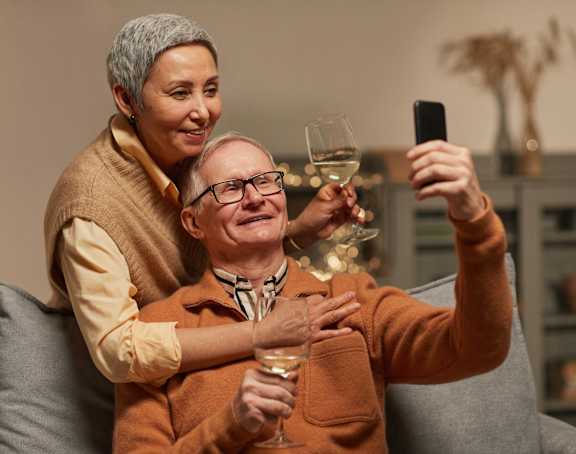 an older man sitting on a couch with a woman holding a glass of wine